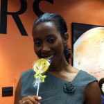 Woman smiling with a Sudsies smiley cookie in front of Mars exhibit