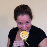 Woman smiling while playfully biting a wrapped Sudsies smiley cookie