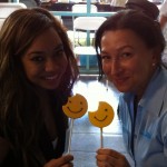 Two women smiling with bitten Sudsies smiley cookies